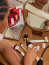 Person selecting ILIA makeup brushes and products from a wooden vanity with a mirror.